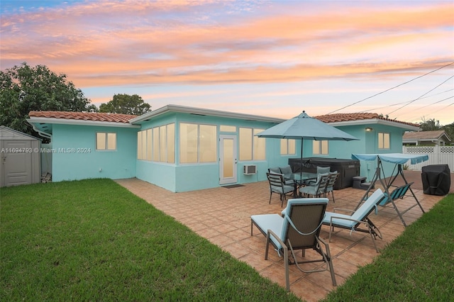 back house at dusk featuring a patio area, a sunroom, a yard, a hot tub, and a storage unit