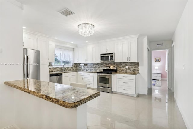 kitchen featuring white cabinets, appliances with stainless steel finishes, kitchen peninsula, and dark stone countertops