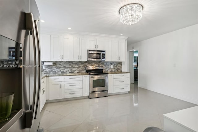 kitchen with white cabinets, dark stone counters, appliances with stainless steel finishes, and a chandelier