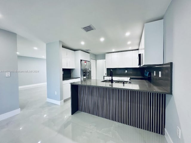 kitchen featuring kitchen peninsula, decorative backsplash, sink, stainless steel fridge with ice dispenser, and white cabinetry