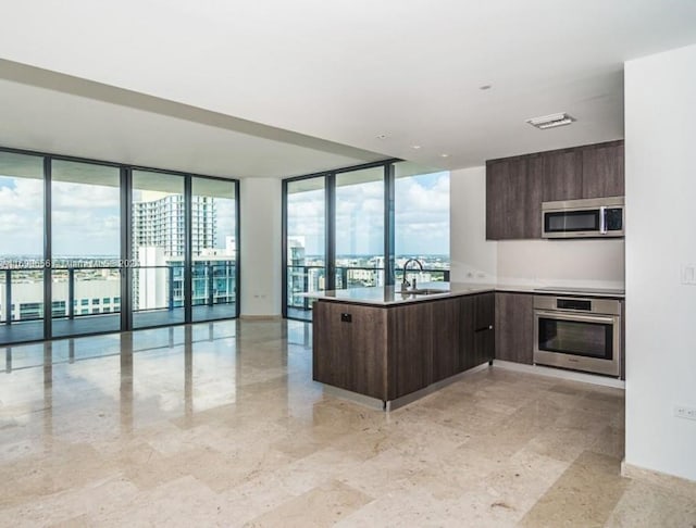 kitchen featuring dark brown cabinetry, floor to ceiling windows, sink, kitchen peninsula, and appliances with stainless steel finishes