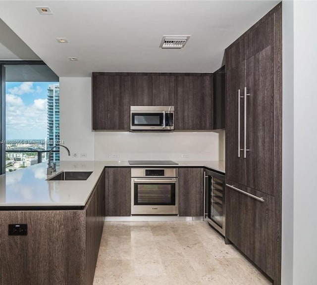 kitchen featuring kitchen peninsula, dark brown cabinets, stainless steel appliances, beverage cooler, and sink