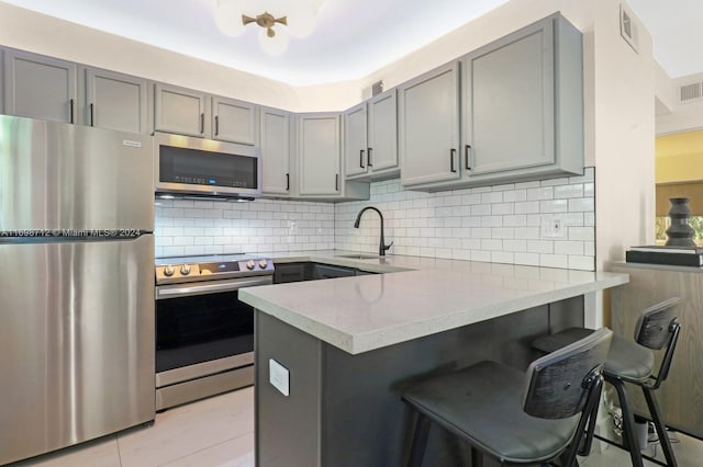 kitchen featuring a kitchen bar, decorative backsplash, kitchen peninsula, stainless steel appliances, and gray cabinets