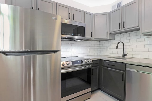 kitchen featuring gray cabinetry, sink, stainless steel appliances, tasteful backsplash, and light stone counters