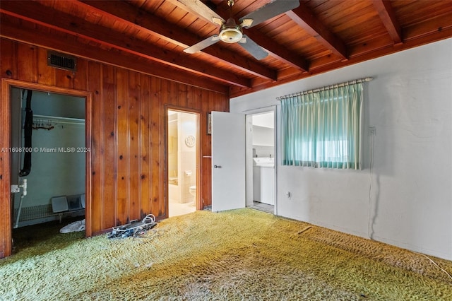 empty room with carpet flooring, ceiling fan, beam ceiling, and wooden walls