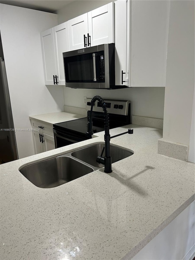 kitchen with white cabinets, light stone countertops, sink, and electric stove