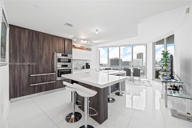 kitchen featuring double oven, a wealth of natural light, white cabinets, and a breakfast bar area