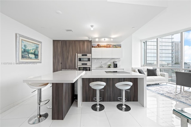 kitchen with decorative backsplash, double oven, white cabinetry, a kitchen island, and a breakfast bar area