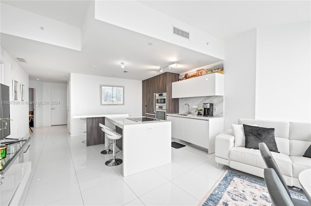 kitchen with a kitchen bar, backsplash, sink, white cabinets, and a center island