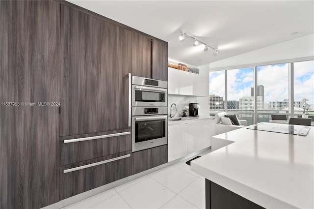 kitchen featuring backsplash, double oven, sink, light tile patterned floors, and lofted ceiling