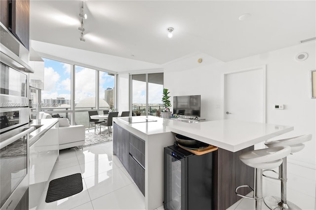 kitchen featuring a center island, beverage cooler, oven, dark brown cabinets, and light tile patterned floors