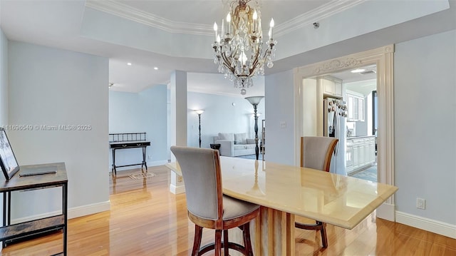 dining area featuring crown molding, a tray ceiling, a chandelier, and light hardwood / wood-style flooring