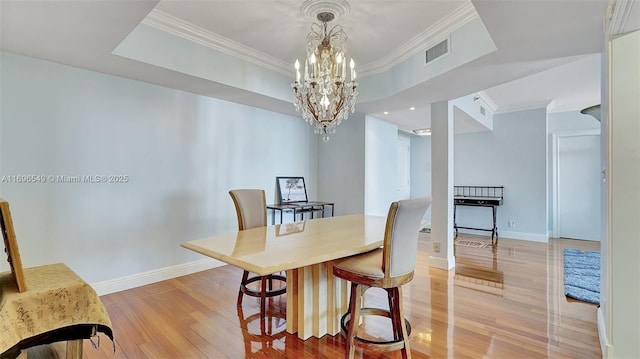 dining area featuring a raised ceiling, crown molding, a chandelier, and light hardwood / wood-style floors