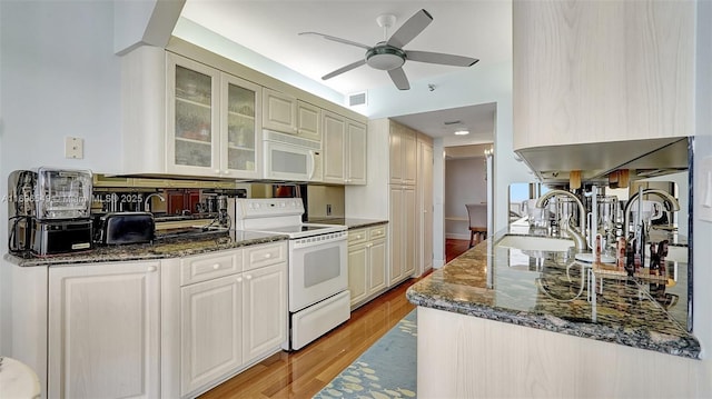 kitchen with sink, white appliances, dark stone counters, and light wood-type flooring