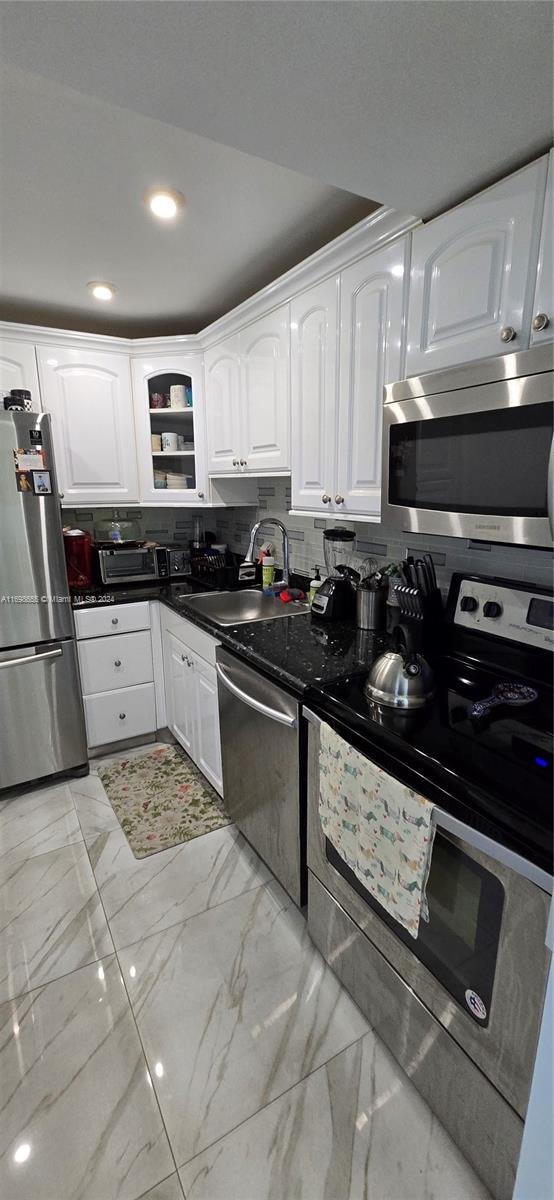 kitchen featuring white cabinets, sink, stainless steel appliances, and dark stone counters