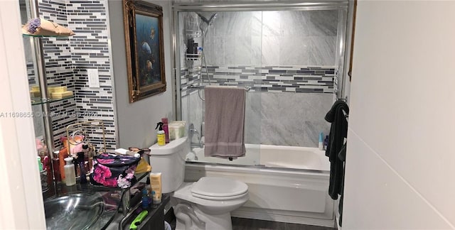 bathroom with toilet, enclosed tub / shower combo, and tile walls