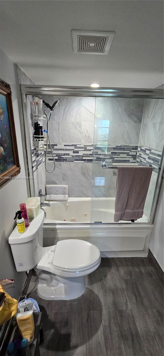 bathroom featuring shower / bath combination with glass door, hardwood / wood-style floors, and toilet