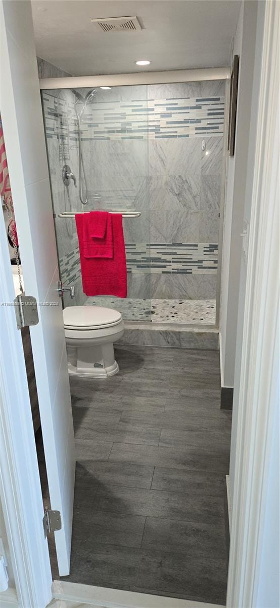 bathroom with hardwood / wood-style floors, toilet, and tiled shower