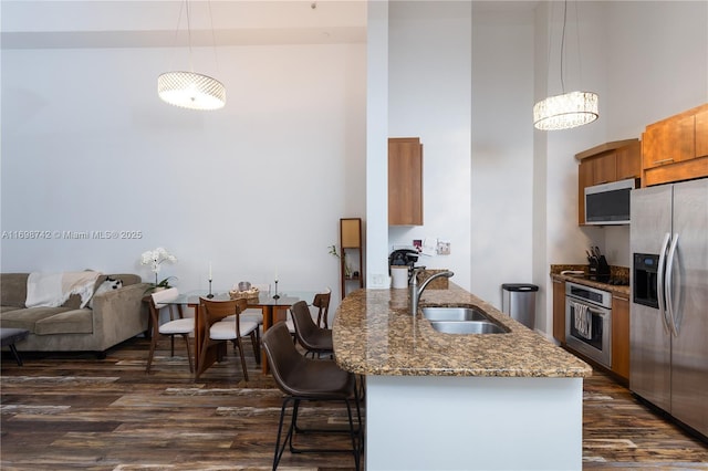 kitchen with dark stone counters, stainless steel appliances, dark wood-type flooring, sink, and hanging light fixtures