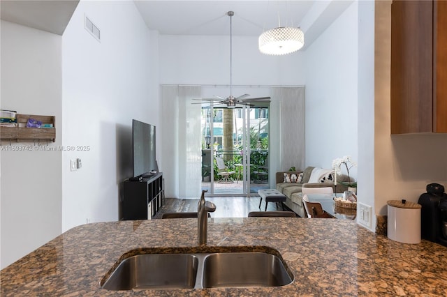 kitchen featuring decorative light fixtures, ceiling fan, dark stone counters, and sink