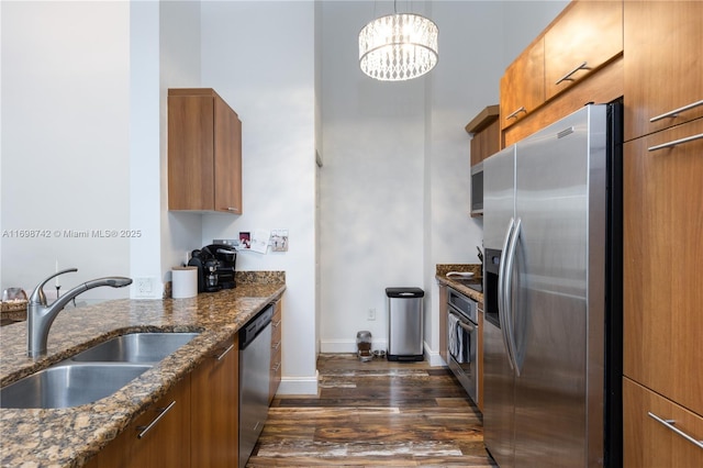 kitchen with stainless steel appliances, sink, a notable chandelier, dark stone countertops, and hanging light fixtures