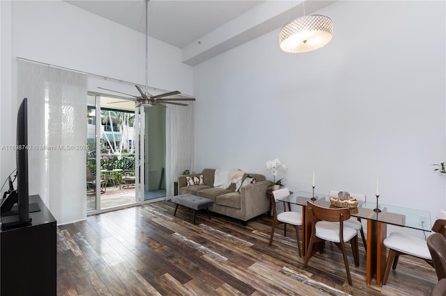 living area with ceiling fan, dark wood-type flooring, and a high ceiling