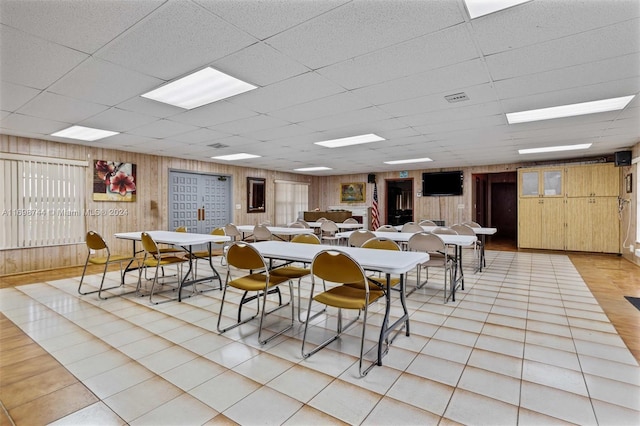 dining space featuring light tile patterned floors, a paneled ceiling, and wooden walls