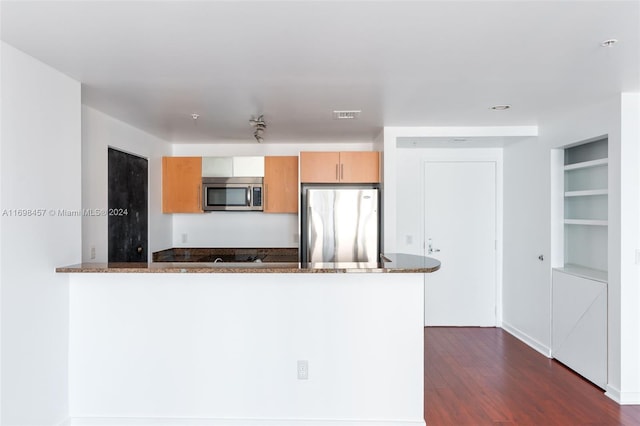 kitchen with dark stone countertops, kitchen peninsula, stainless steel appliances, and dark wood-type flooring