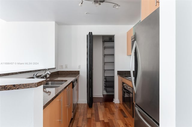 kitchen with stainless steel appliances, dark hardwood / wood-style floors, dark stone counters, and sink