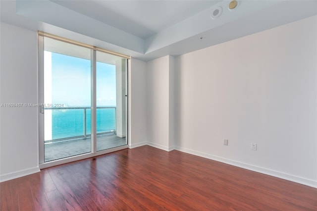 empty room with dark hardwood / wood-style floors, a water view, and a wealth of natural light