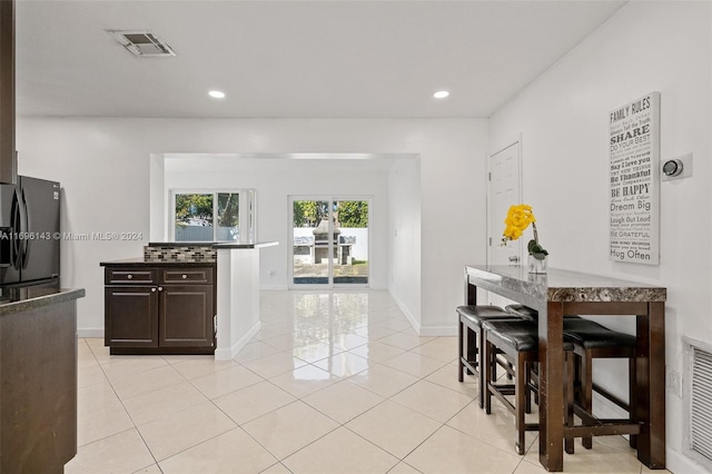 kitchen with black refrigerator, dark brown cabinetry, and light tile patterned flooring