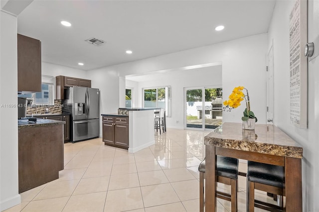 kitchen featuring dark brown cabinetry, backsplash, stainless steel fridge, a breakfast bar, and a kitchen island