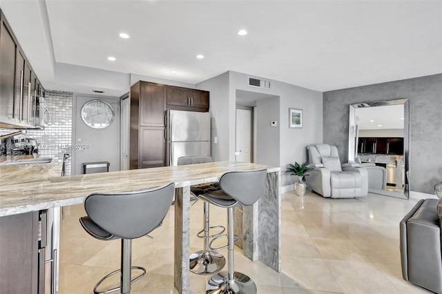 kitchen with sink, stainless steel fridge, light tile patterned flooring, a kitchen bar, and dark brown cabinetry