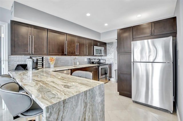 kitchen with decorative backsplash, light stone counters, appliances with stainless steel finishes, a kitchen bar, and kitchen peninsula