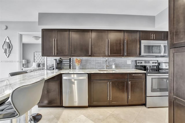 kitchen featuring sink, stainless steel appliances, light stone counters, backsplash, and dark brown cabinets