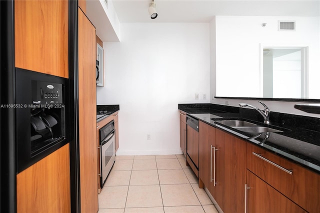 kitchen with light tile patterned floors, stainless steel appliances, dark stone counters, and sink