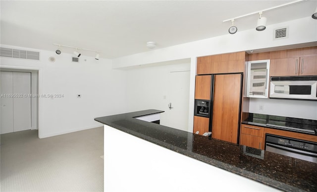 kitchen with stainless steel oven, cooktop, built in fridge, kitchen peninsula, and dark stone counters