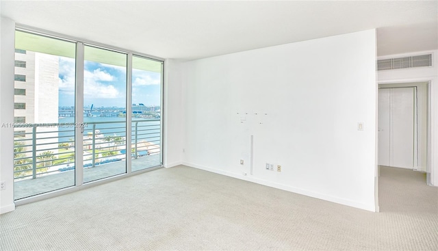 unfurnished room featuring a water view, a wall of windows, and light colored carpet