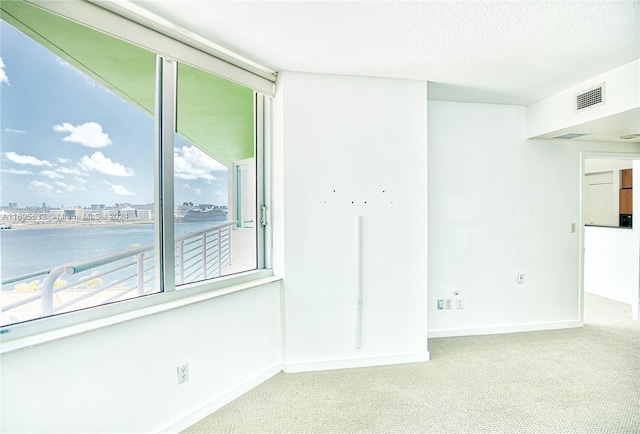 unfurnished room with carpet flooring, a water view, and a textured ceiling