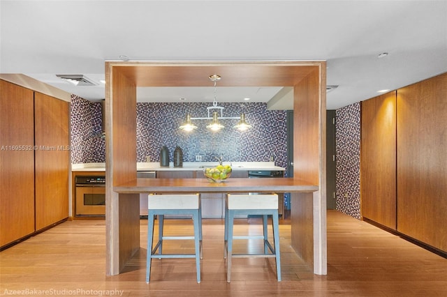 kitchen featuring decorative backsplash, appliances with stainless steel finishes, hanging light fixtures, and light wood-type flooring