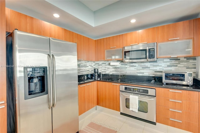 kitchen with light tile patterned flooring, stainless steel appliances, decorative backsplash, and dark stone countertops