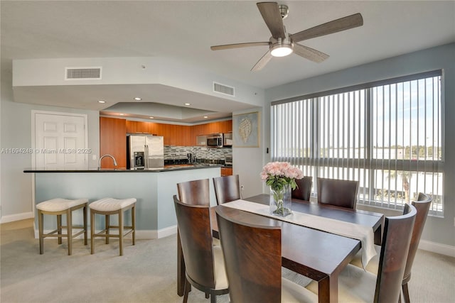 carpeted dining space with a raised ceiling, sink, and ceiling fan