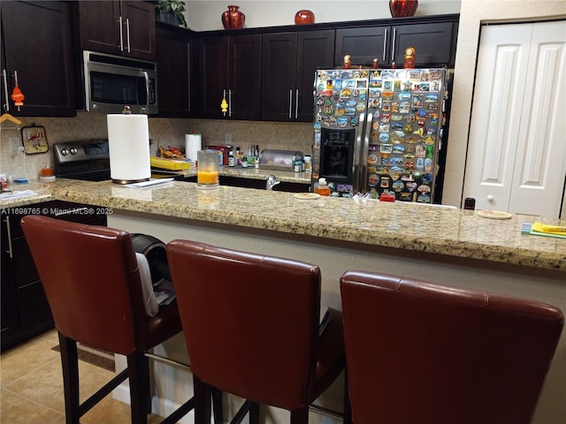 kitchen featuring stainless steel appliances, light stone counters, tasteful backsplash, and light tile patterned flooring