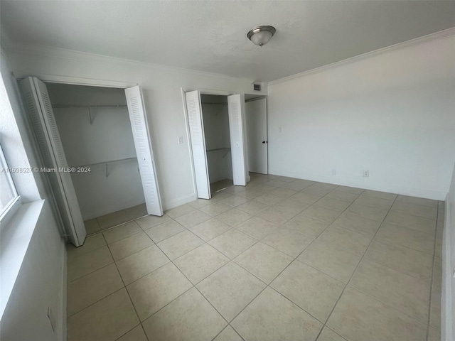 unfurnished bedroom featuring light tile patterned flooring, crown molding, and multiple closets