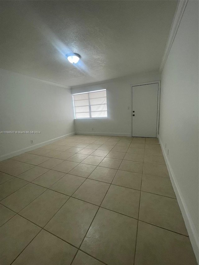 spare room featuring a textured ceiling, ornamental molding, and light tile patterned flooring