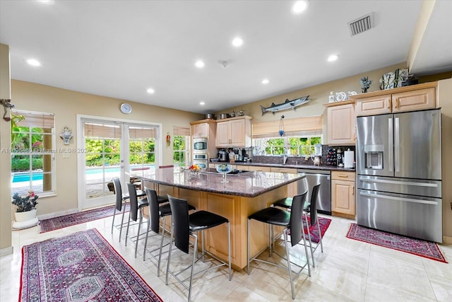 kitchen with a kitchen island, a healthy amount of sunlight, appliances with stainless steel finishes, and dark stone counters