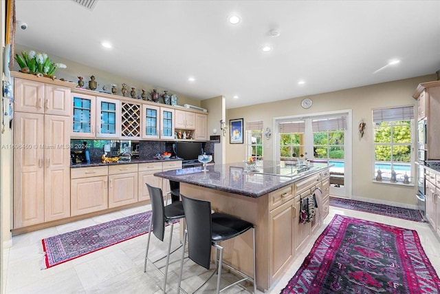 kitchen with a center island, tasteful backsplash, dark stone counters, a kitchen bar, and light brown cabinetry