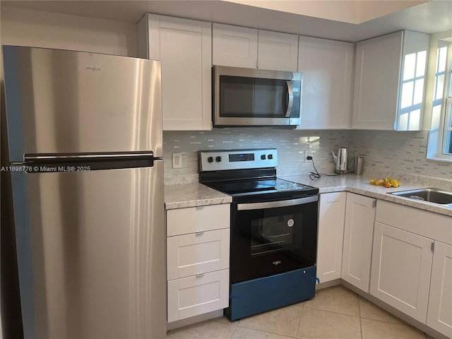 kitchen with appliances with stainless steel finishes, sink, light tile patterned floors, and white cabinets