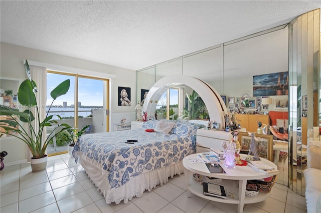 bedroom featuring access to outside, a textured ceiling, a water view, and light tile patterned floors