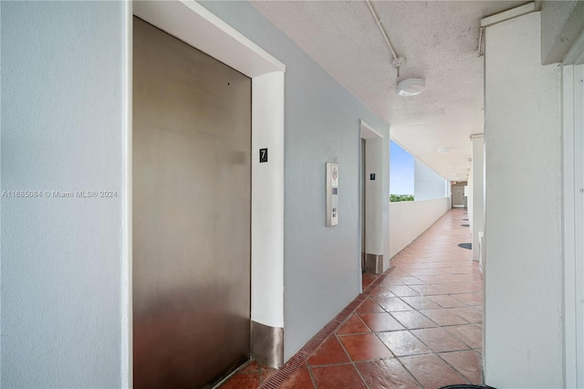 hall featuring tile patterned flooring, a textured ceiling, and elevator